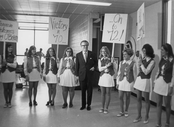 Larry Frances O'Brien, Jr. campaigning with group of women in matching outfits holding signs that say, "Victory in '70," "Wisconsin welcomes O'Brien," and "...On to '72!." O'Brien was elected in 1968 and 1970 as the Democratic National Committee Chairman.