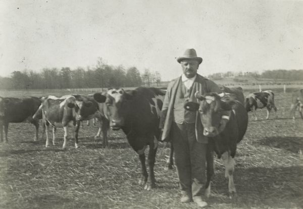 Governor Emanuel Philipp with his arm around a cow. He is standing in a field with several other cows.