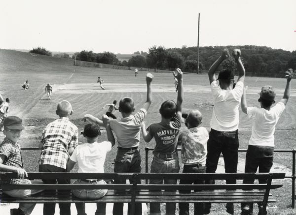 Young fans cheer as a runner races home on a grounder to short during a Mayville Recreation Department baseball game.