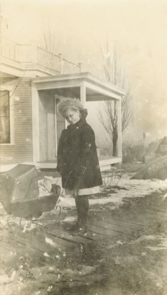Anna Ely, later Anna Ely Morehouse, wearing a military jacket and pushing a baby carriage on a wooden sidewalk.