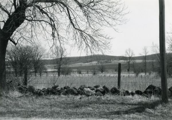Kettle Moraine State Forest with moraines. A fence line partially consisting of glacial erratic rocks is visible in the foreground.