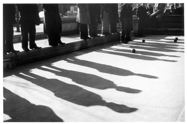 Group of men playing boccie, with their shadows casting over the game on East Houston Street.