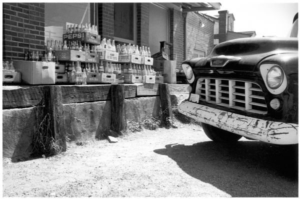 Stacked crates of bottles near a parked automobile.