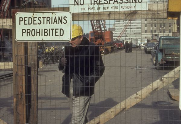 Man with hard hat walking behind a fence, possibly an architect, at the construction site of The World Trade Center.