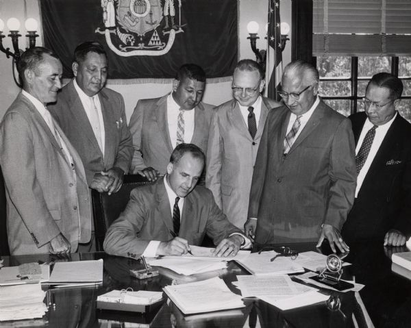 Governor Gaylord Nelson signing the bill which created Menominee County as the state's 72nd county. The new county consisted of those portions of Shawano and Oconto counties that were part of the Menominee Reservation. Watching left to right are Gordon Dickie, Bernard Grignon, Hilary Waukau, Attorney General John W. Reynolds. James Frechette, and Al Dodge.