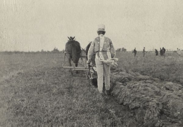 Man wearing an Uncle Sam costume plowing with a team of horses for an agricultural extension demonstration.  It is likely the event took place during World War I to publicize the importance of agriculture to the war effort.