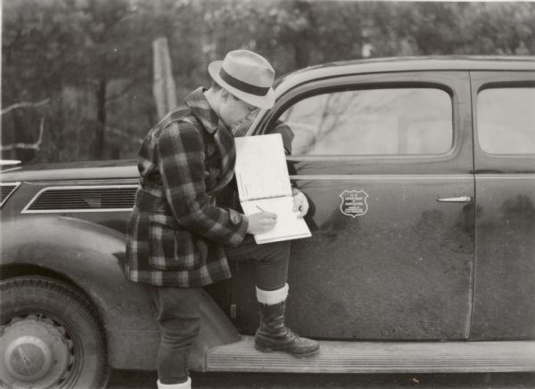 Eradication of the blister rust threat to Wisconsin's white pine forest created a joint federal-state effort that was almost military in its proportions. Here Ray Weber, a supervisor of an eradication crew, records work done on time sheets.