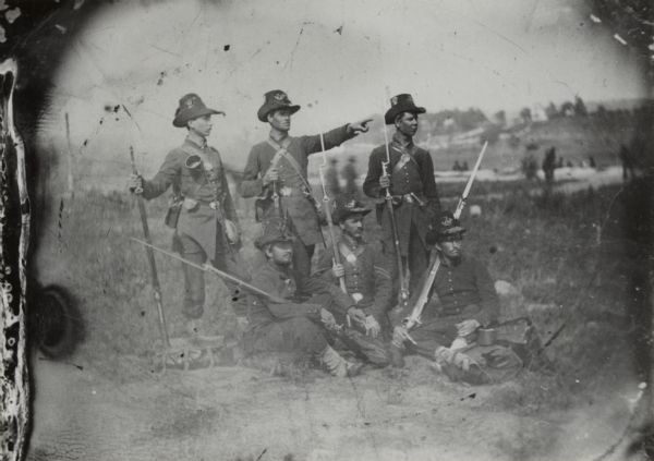 Six Wisconsin soldiers that were part of the Iron Brigade, a unit comprised of soldiers from Wisconsin, Indiana, and Michigan that was known for its determined fighting ability. This group has been tentatively identified as members of Co. C of the 2nd Wisconsin, and the individual seated in the center is thought to be Corporal Spencer Train. All of the soldiers are wearing the black Hardee hats, frock coats, and leggings characteristic of the Iron Brigade, and it may be that the photograph was taken soon after the uniforms were issued to show the men fully equipped. If the corporal is indeed Train, the picture was taken between October 1861, when blue uniforms replaced the gray originally issued by the state of Wisconsin and August 1862, when Train was promoted to sergeant. Train died in 1863 from wounds received at Gettysburg.