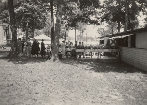 Summer camp for Wisconsin farm women on the grounds of the Wisconsin State Fair, with Wisconsin home economics leader Nellie Kedzie Jones. Mrs. Jones is probably the woman near the tree with her back to the camera.