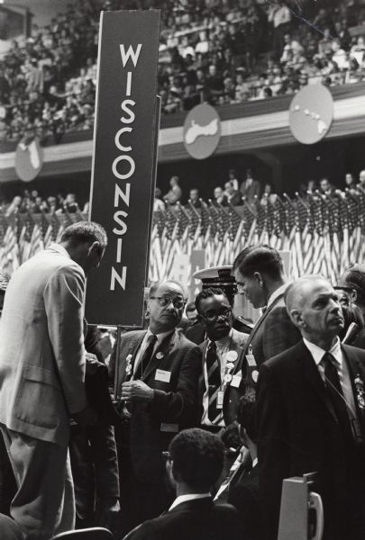 Several members of the Wisconsin delegation who support Eugene McCarthy, gather around the state sign at the National Democratic Convention.  Only Hilton Hanna, an African American, has been identified.