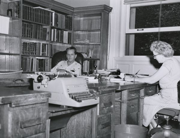 Wisconsin Historical Society archivist Jesse Boell, later the archivist of the University of Wisconsin, seen in his office on the third floor of the Historical Society building.  The woman in the photograph is unidentified.