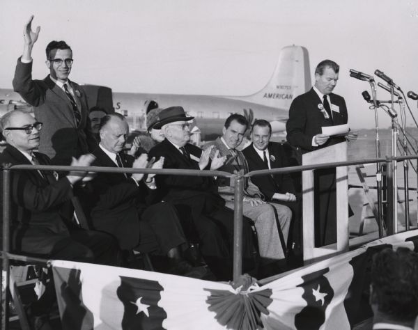 The speakers platform during a Presidential campaign rally for Richard M. Nixon at Billy Mitchell Airport in Milwaukee. With Nixon on the platform are Kirby Hendee (standing), a congressional candidate; Senator Alexander Wiley (wearing the hat); and Philip G. Kuehn (to the vice-president's left), the Republican candidate for governor. Richard S. Falk, chairman of arrangements is making the introductions. Also seen are Fred Eaton (extreme right), Secretary of the Interior, and Vincent A. Mercurio, chair of the Milwaukee County Republican Party.