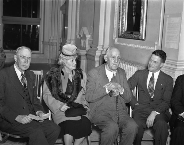 Clifford L. Lord, director of the State Historical Society (on the right), seated with Governor Walter Goodland and Mrs. Goodland at an event at the Wisconsin Historical Society.  The view shows the first floor lobby prior to remodeling.