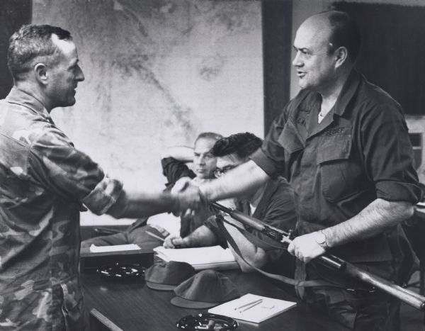 Secretary of Defense Melvin Laird, wearing a fatigue uniform, shaking hands with a military officer during a tour of Vietnam.
