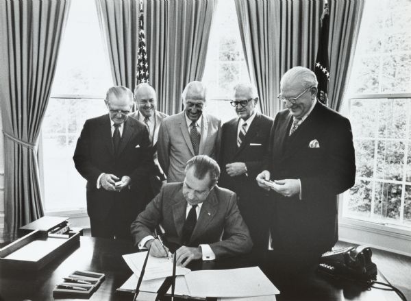 President Nixon signs a draft bill in the Oval Office of the White House while Secretary of Defense Melvin Laird (second from the left) and others watch. This bill extended the draft and increased military pay.
