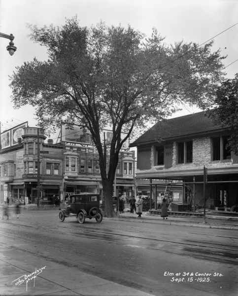 Automobile parked in front of large elm tree at the corner of N. 3rd and W. Center Streets.