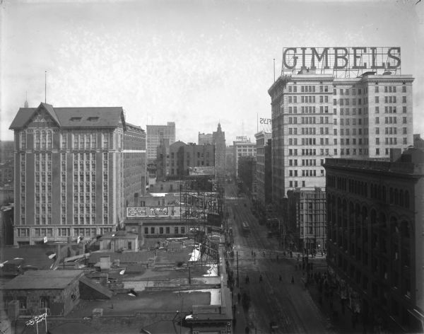 Elevated view looking east on W. Wisconsin Avenue from approximately N. 4th Street, with the Wisconsin Hotel on the left and the Majestic building on the right with a Gimbels sign on the roof.