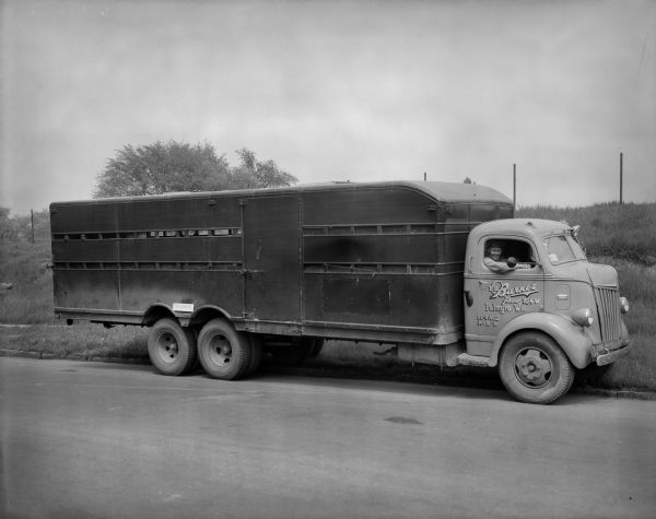 E.H. Barnes livestock truck pulled over on the side of a country road. A male driver is looking out of the passenger side of the truck.