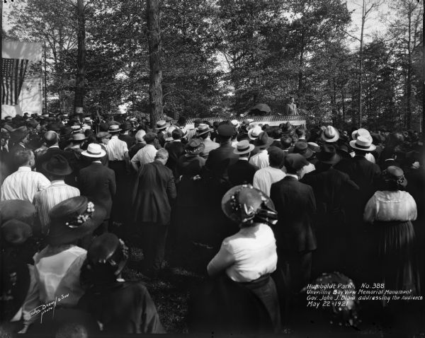 Crowd of spectators attend a dedication ceremony for a World War I monument in Humboldt Park. Caption on glass plate reads, "Humboldt Park, Unveiling Bay View Memorial Monument. Gov. John J. Blain addressing the audience".