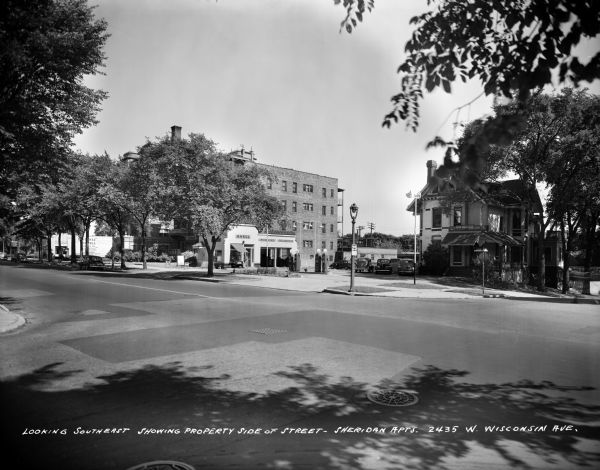 The Sheridan Apartment building at 2435 W. Wisconsin Avenue. Caption on glass plate reads: "Looking southeast showing property side of street — Sheridan Apartments, 2435 W. Wisconsin Ave." There is a Shell Gas Station on the corner.
