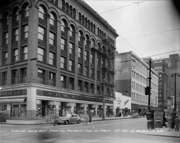 F.W. Woolworth Company and other commercial buildings on the southwest corner of N. 3rd Street and W. Wisconsin Avenue. Pedestrians are walking on the sidewalks. Caption on print reads: "Looking southwest showing property side of street, 317-321 W. Wisconsin Ave."