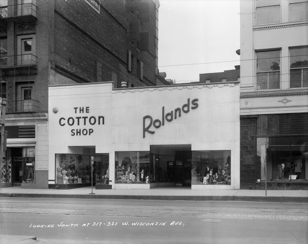 The Cotton Shop and Rolands on W. Wisconsin Avenue. Caption on print reads: "Looking south at 317-321 W. Wisconsin Ave". Plaque on building next door reads: "Boston Store - The Heart of Milwaukee".