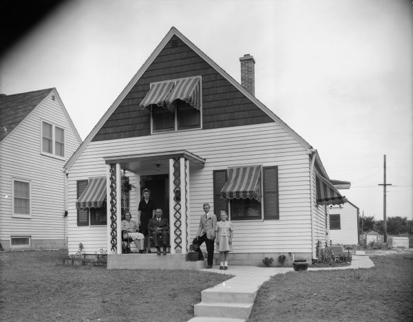 Residental neighborhood, with family posing on the front steps of a new Cape Cod style home.
