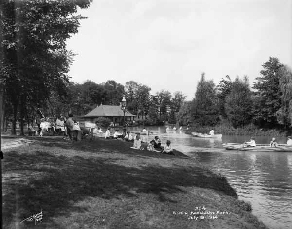 Individuals boating in the Kosciusko Park lagoon, with onlookers sitting on the bank. Caption on glass plate reads: "Boating, Kosciusko Park".