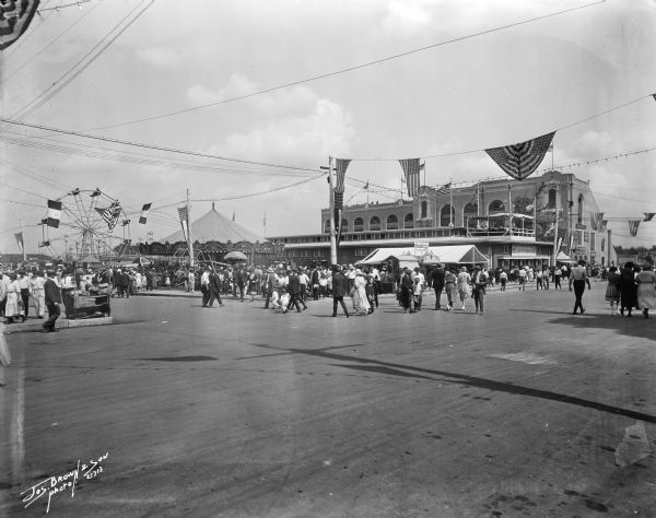 Crowds of people walking, with amusement rides in the backround. Presumably the Wisconsin State Fair.