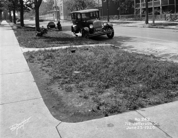 Automobile and motorcycle with sidecar parked on the side of the road at 712 Jefferson Street, near E. Ogden Avenue. The Notre Dame convent is visible in the background.