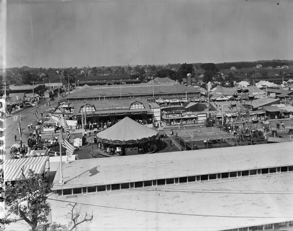 Elevated view of the Wisconsin State Fair looking west from the top of the grandstand. Amusement rides and pavilions visible with individuals walking.