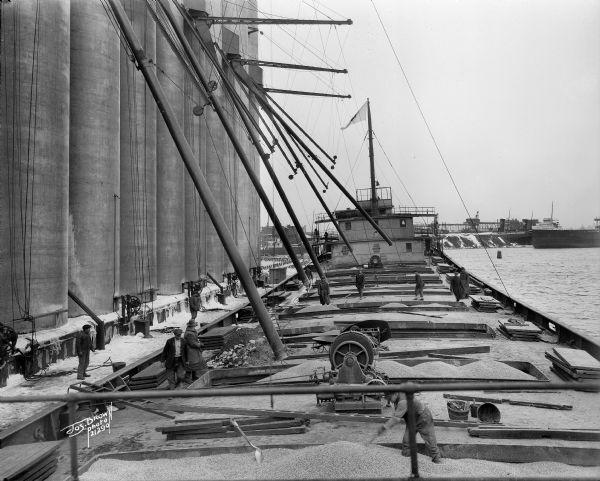 Workers shoveling grain, possibly corn, onto a lake vessel. Probably on the lower Milwaukee River.