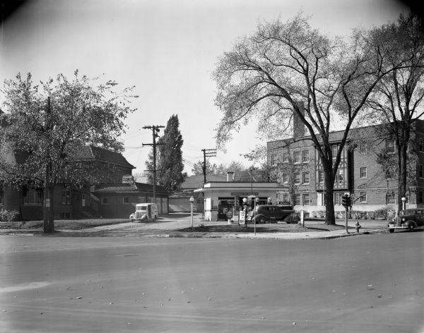 View across intersection towards a man standing next to automobile at a service station at the corner of W. Libson Avenue and W. Sherman Boulevard. The Clasen Funeral home is at 4312 W. Lloyd Street at N. 44th Street.