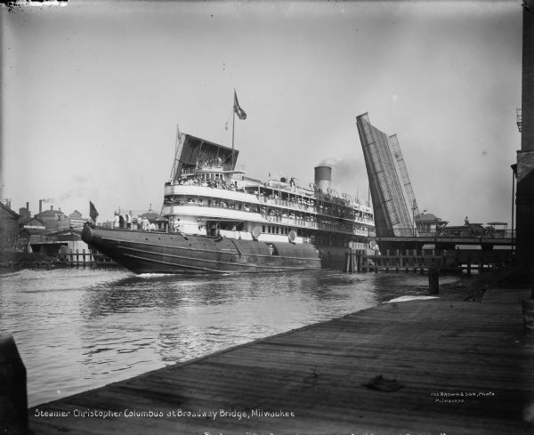 The excursion steamer "Christopher Columbus" passing through the Broadway Bridge in Milwaukee, Wisconsin. Caption on glass plate reads, "Steamer, Christopher Columbus at Broadway Bridge, Milwaukee."
