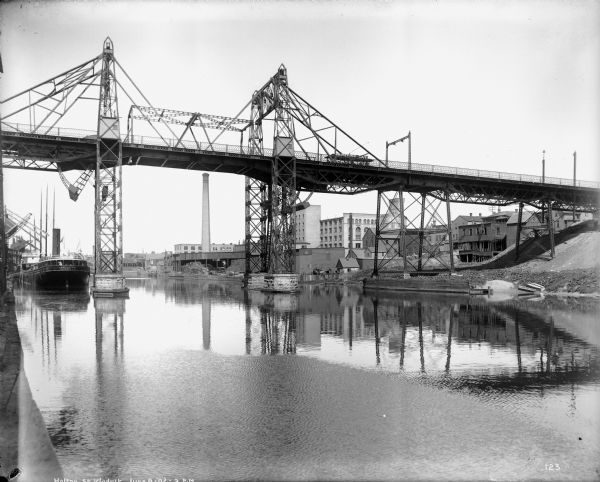 Looking up the Milwaukee River to the Holton Street viaduct. In the center is the Gallun tannery. There is also a steamboat in the harbor, several lumber yards, and factories.