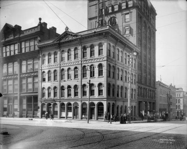 Herold Newspaper building and surrounding commercial area at the southwest corner of Broadway and Mason Street. Pedestrians are crossing the street, and horse-drawn vehicles are parked at the curb.
