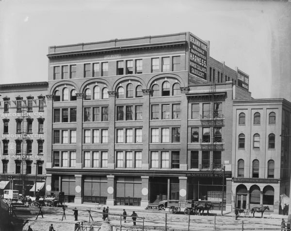 Elevated view of the Joys Building, located on the west side of N. Water Street between E. Buffalo and E. Chicago Streets. Several horse-drawn vehicles are parked in front of the building.