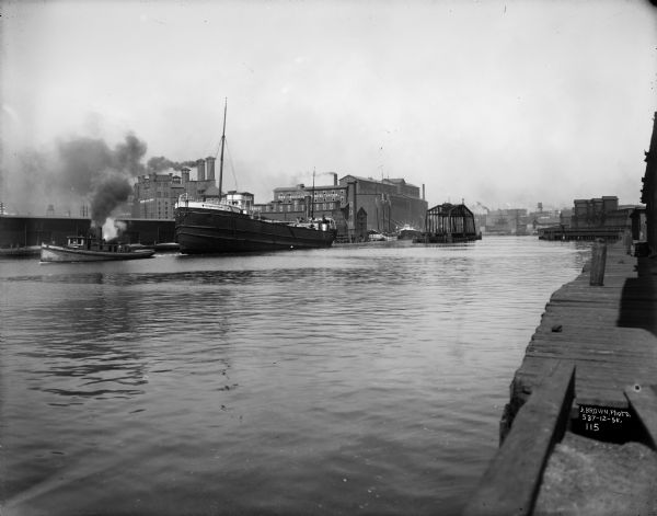 Steamboat "Thomas Mattham" in the Milwaukee harbor being pulled by a tugboat from the north bank near Erie Street.