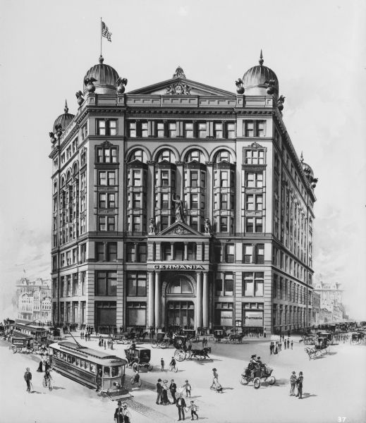 Germania Building with streetcars, automobiles, and pedestrians on the south side of W. Wells Street between N. Plankinton Avenue and N. 2nd Street.
