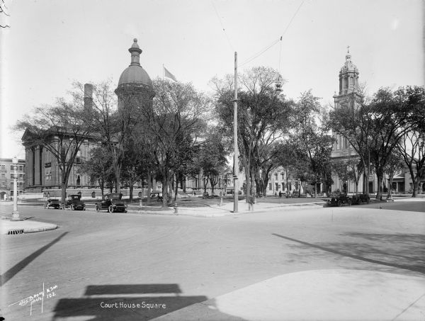 Courthouse (now Cathedral) Square, looking northeast from N. Jefferson and E. Wells Street. People are sitting on benches in the park, with the courthouse in the background. Caption on glass plate reads: "Court House [<i>sic</I>] Square".