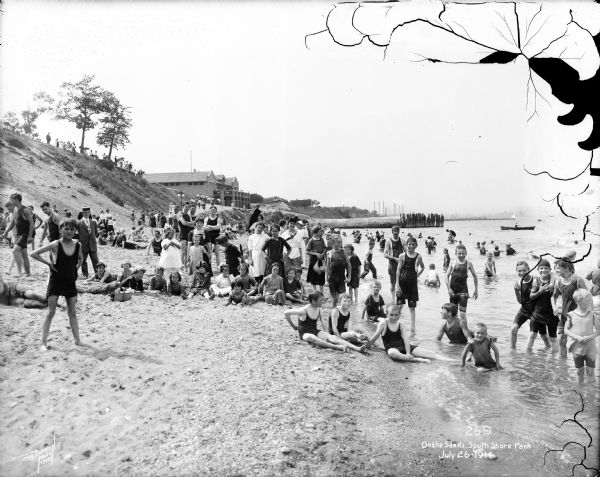 A group, mostly youth, on the shores of Lake Michigan at South Shore beach in the Bay View neighborhood. Caption on glass plate reads, "On the Sands, South Shore Park".