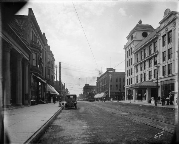 Looking south on N. 3rd Street from just north of W. North Avenue. On the right is the future Rosenberg's clothing store. Automobiles are parked at the curb, and pedestrians are on the sidewalk.