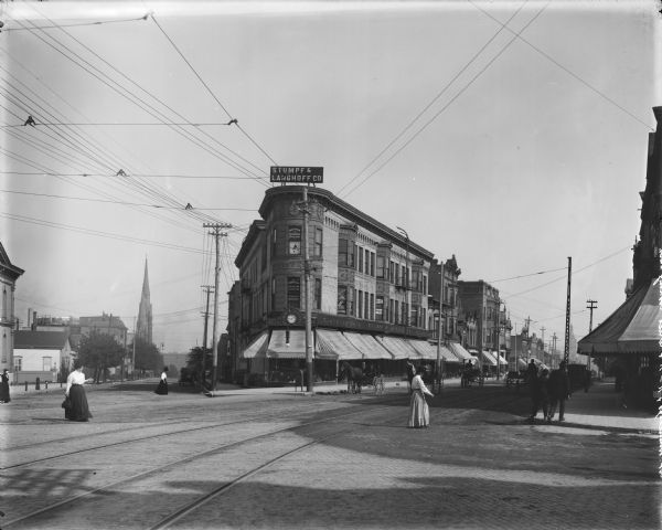 Looking southeast on Winnebago Street, and east on W. Vilet Street from N. 11th Street. Stumpf and Langhoff Co. clothing store from the corner of Winnebago and 11th Street. Horse-drawn vehicles and pedestrians are on the street.