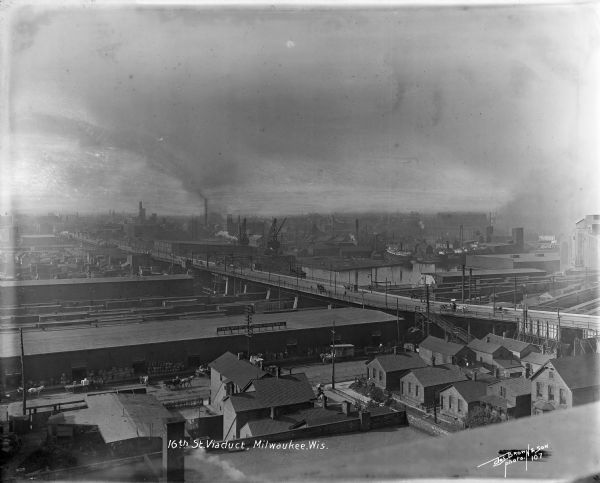 Looking south towards the 16th Street viaduct over Menominee Valley from about Clybourn Street. Shows the surrounding industrial area and neighborhoods. Several horse-drawn vehicles are crossing the bridge.
