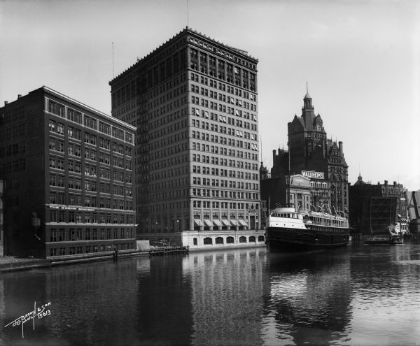 Looking south from Wells Street. A boat travels along the Milwaukee River in the foreground. Landmarks left to right: Manufacturers Home Building, First National Bank, and the Pabst Building. Caption on glass plate reads: "View S. from Oneida St. Bridge".
