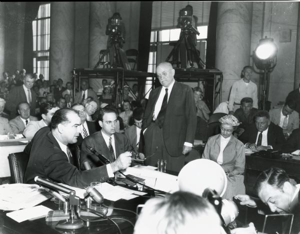 Senator Joseph R. McCarthy of Wisconsin during the Army-McCarthy hearings, with committee counsel Roy Cohn next to McCarthy and Republican Senator Ralph Flanders of Vermont standing at the center. Flanders, who was taking the lead in an effort to depose McCarthy, had just delivered a letter to McCarthy informing him that he intended to introduce a resolution to censure McCarthy.  Here McCarthy responds saying that Flanders should take the witness stand if he has any information about the "Army-McCarthy row other than the 'usual smears... from the smear sheets.'"  Flanders' original motion called for McCarthy to be stripped of his committee post.  A revised motion eventually led to McCarthy's condemnation by the Senate.  
