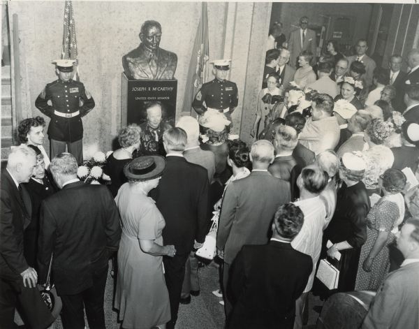 Dedication of the Joseph R. McCarthy Memorial in the Outagamie Counthouse on the second anniversary of the senator's death.  Directly in front of the bust is sculptor Suzanne Stevenson.  The chief speaker was Senator Styles Bridges, in the left foreground with his back to the camera.  Mrs. McCarthy, who is not visible in this photograph, told the crowd of 400-500 people that thousands of individuals had contributed to the memorial. In 2001 the bust was moved to the Outagamie County Historical Society.