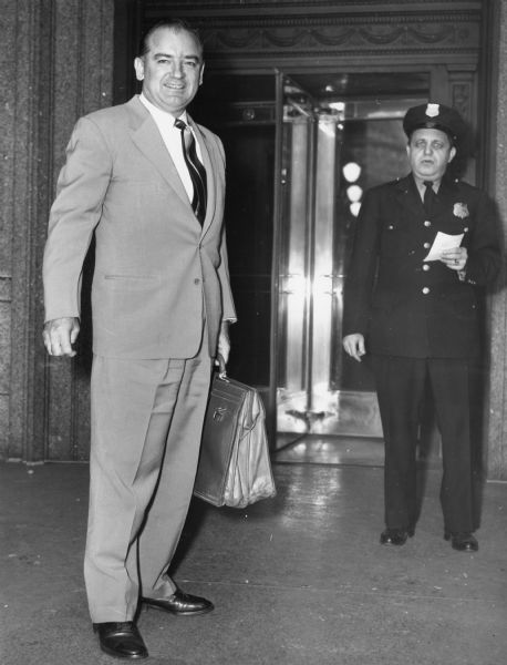 Senator Joseph R. McCarthy, now chair of the Senate Investigating Committee, arrives at a New York City hotel to begin hearings on alleged Communist espionage within the Army Signal Corps Laboratory located at Fort Monmouth, New Jersey.  As usual, McCarthy had with him a briefcase bulging with documents.  The original caption distributed to the media with this photograph stated that "three persons reportedly named as being involved in the ring were to be questioned by the senator, who said that the trio was named by a mystery witness who promised to 'tell all' about the spy group."  As usual McCarthy released information to the press to advance his own purposes.