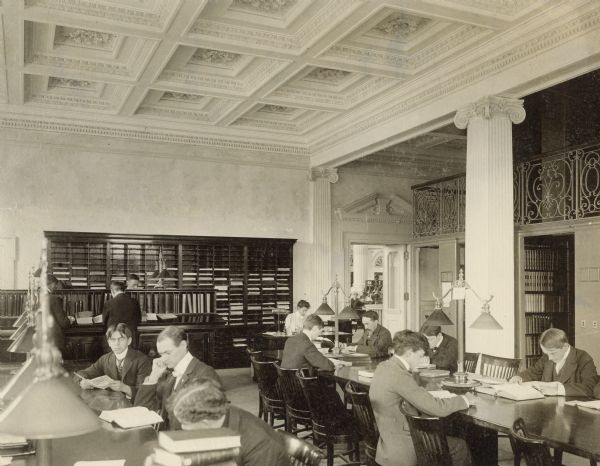SHSW Periodical Reading Room, showing mezzanine stacks, original tables and lamps, and coffered ceiling treatment. Among the University of Wisconsin students seated at the tables is Charles McCarthy (fourth from right), head of the Legislative Reference Bureau.
