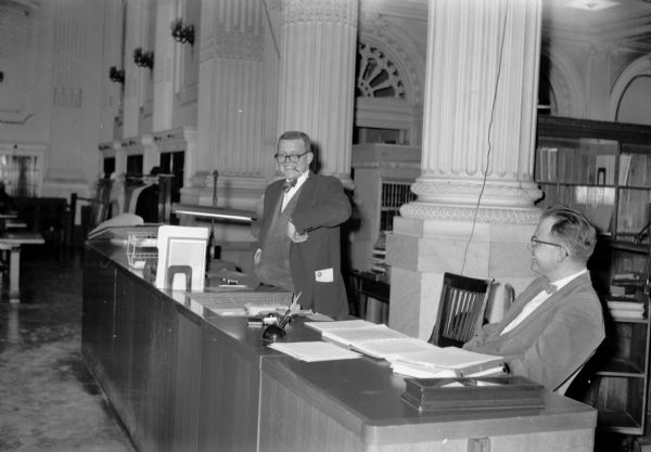 Library staff members at the new consolidated service desk in the Historical Society Library Reading Room.  Microfilm cubicles have not yet been installed and the original light fixtures on the walls may be seen in the background.